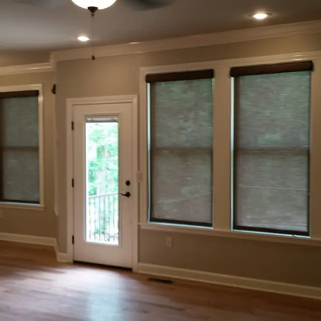 Two installed cellular roller shades beside a glass door in a taupe walled room