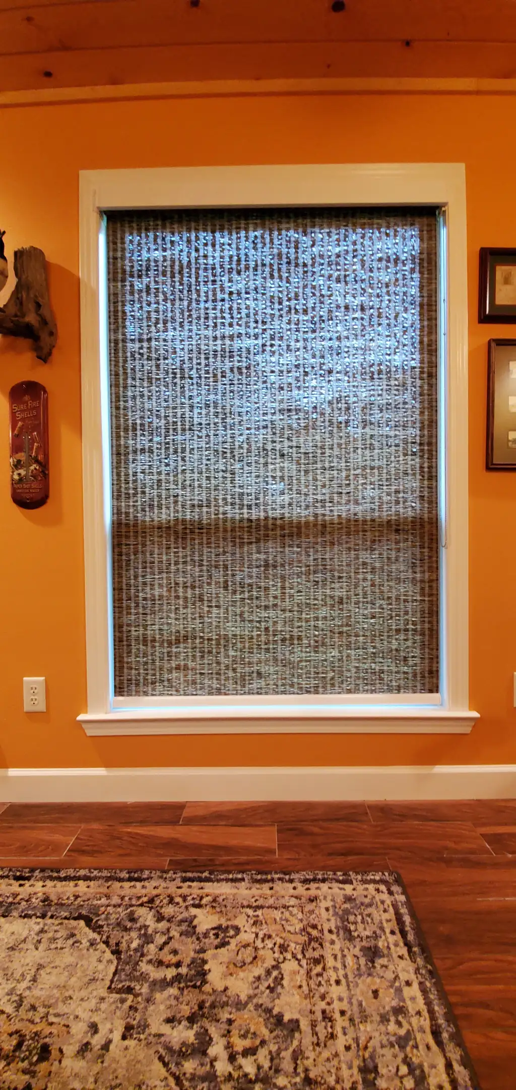 A woven natural roller shade in a rustic room with wood ceiling and warm walls