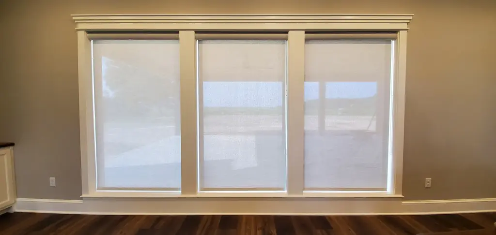 Solar shades lowered across a bank of three windows in a neutral living room