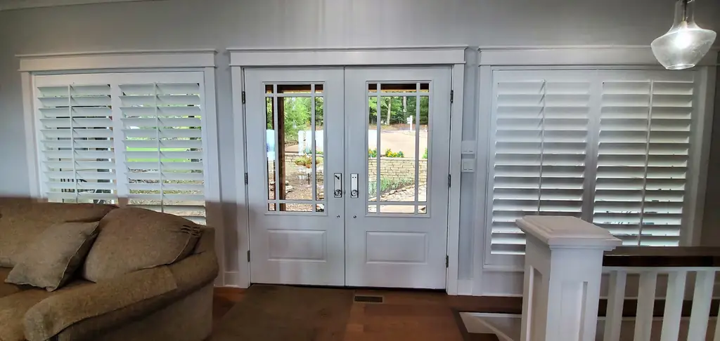 Plantation shutters flanking a white French door entry with a staircase beyond