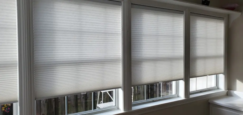 Three cellular honeycomb shades drawn across tall sunroom windows